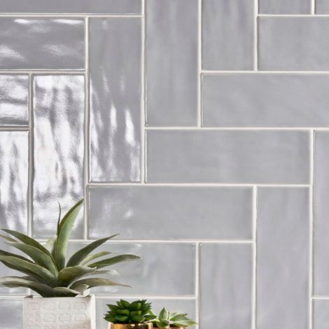 A potted plant is sitting on a table in front of a wall of tiles.