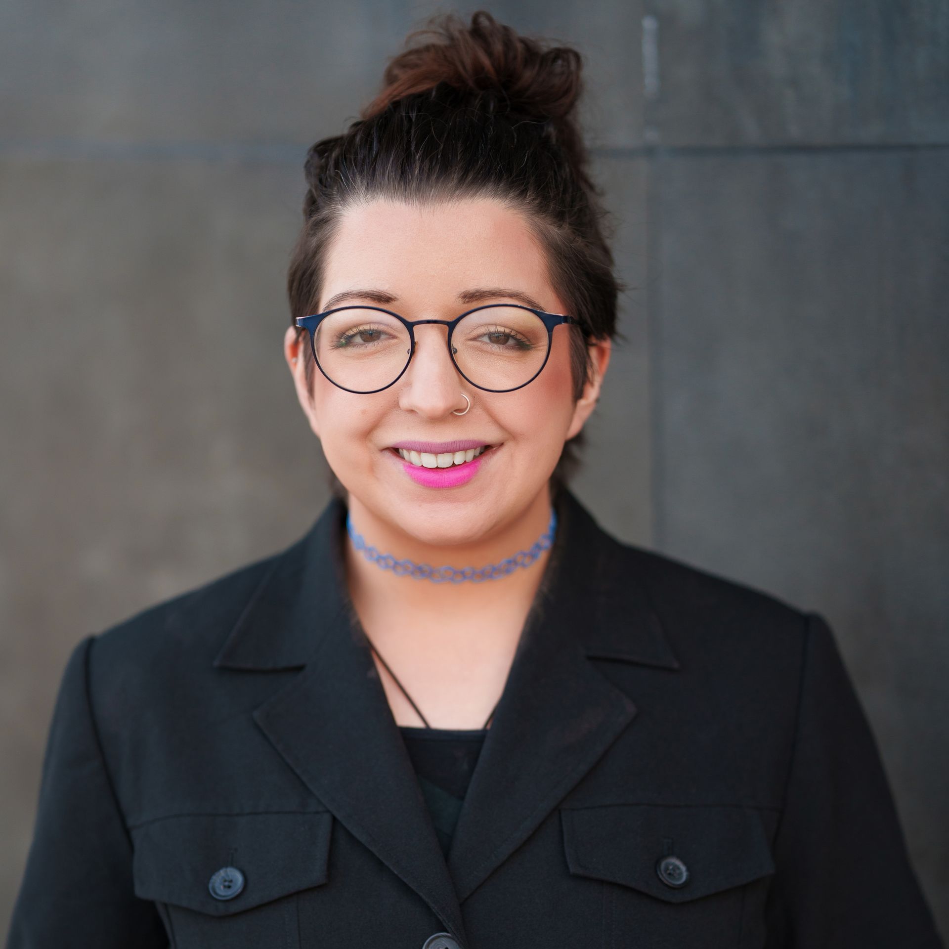 A woman wearing glasses and a black jacket smiles for the camera