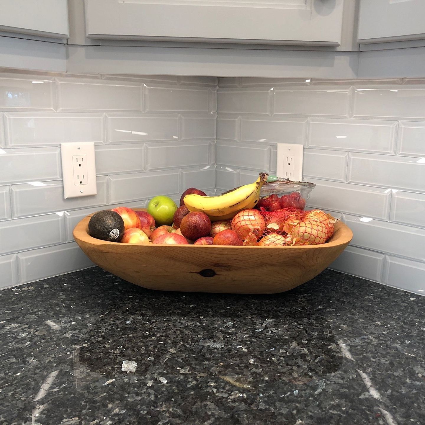 A wooden bowl filled with fruit and vegetables on a counter.