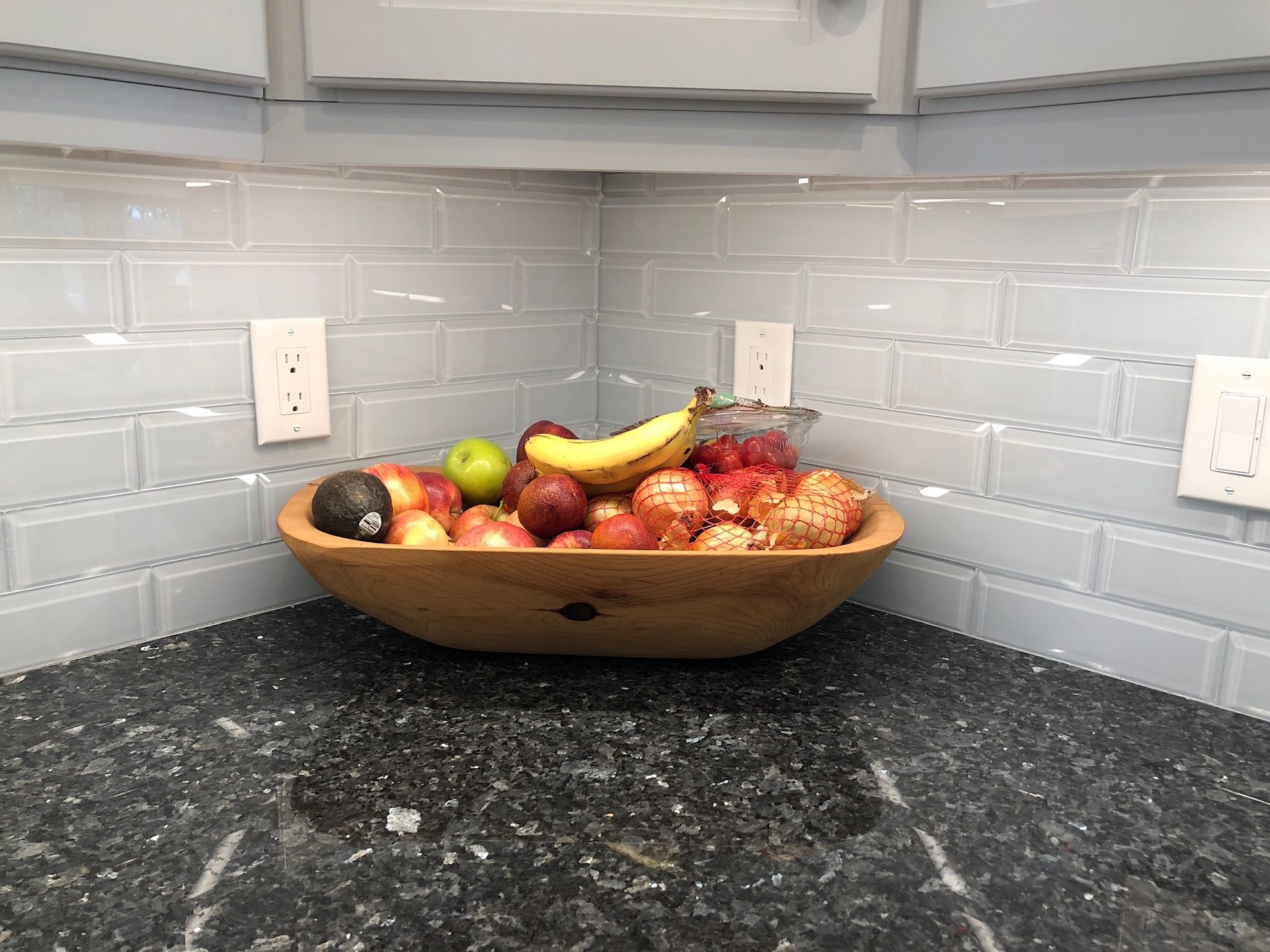 A wooden bowl filled with fruit is on a counter in a kitchen.