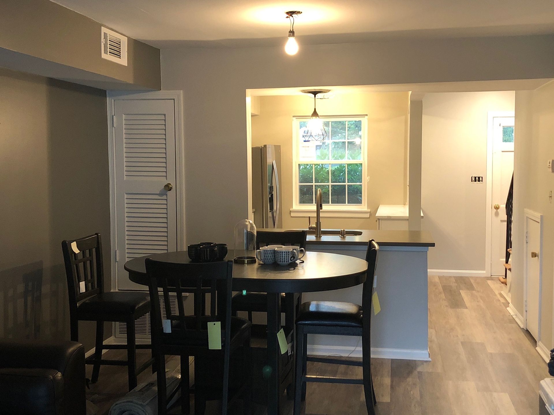 A dining room with a table and chairs and a kitchen in the background.