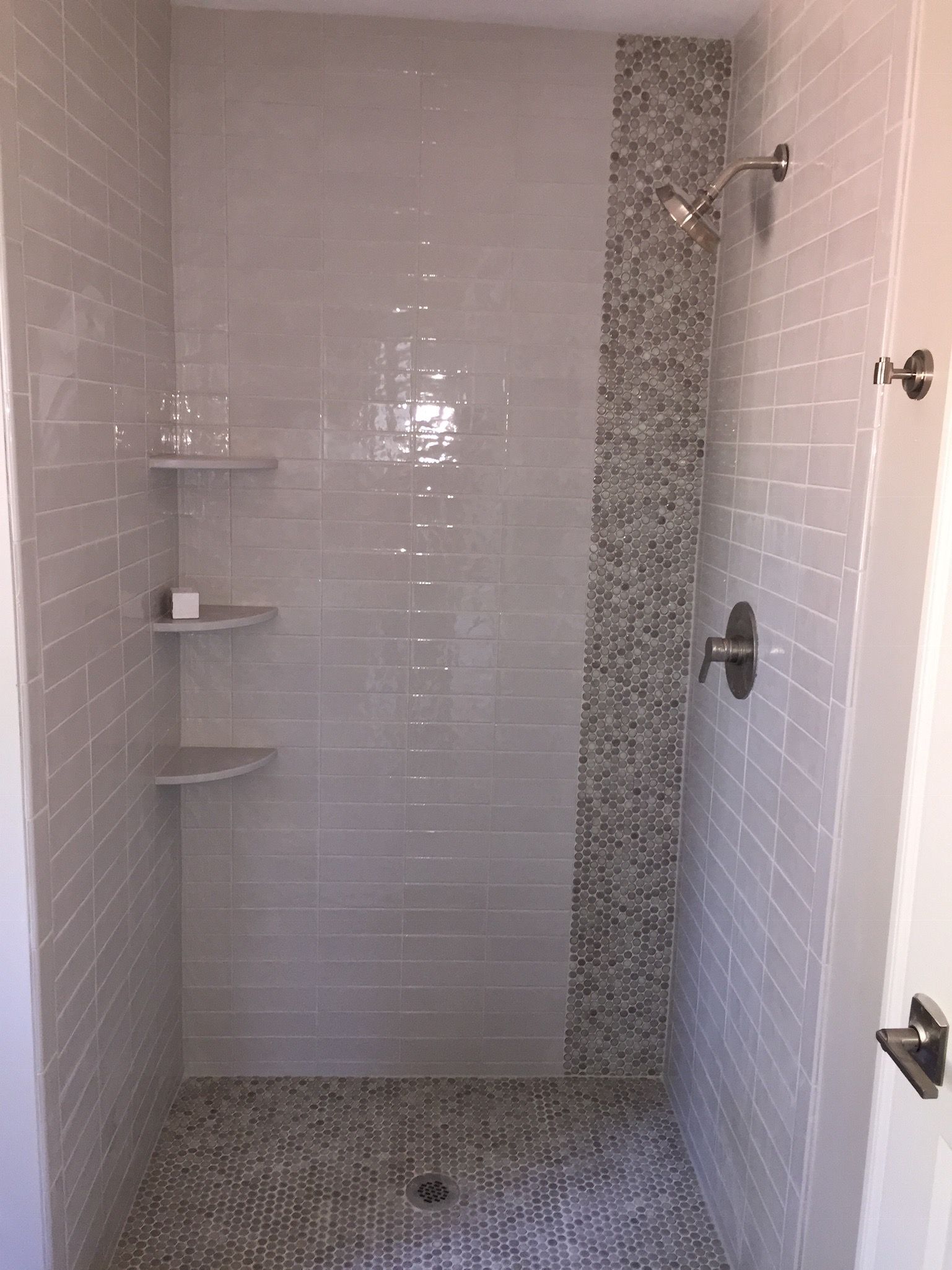 A walk in shower with white tiles and a mosaic wall.