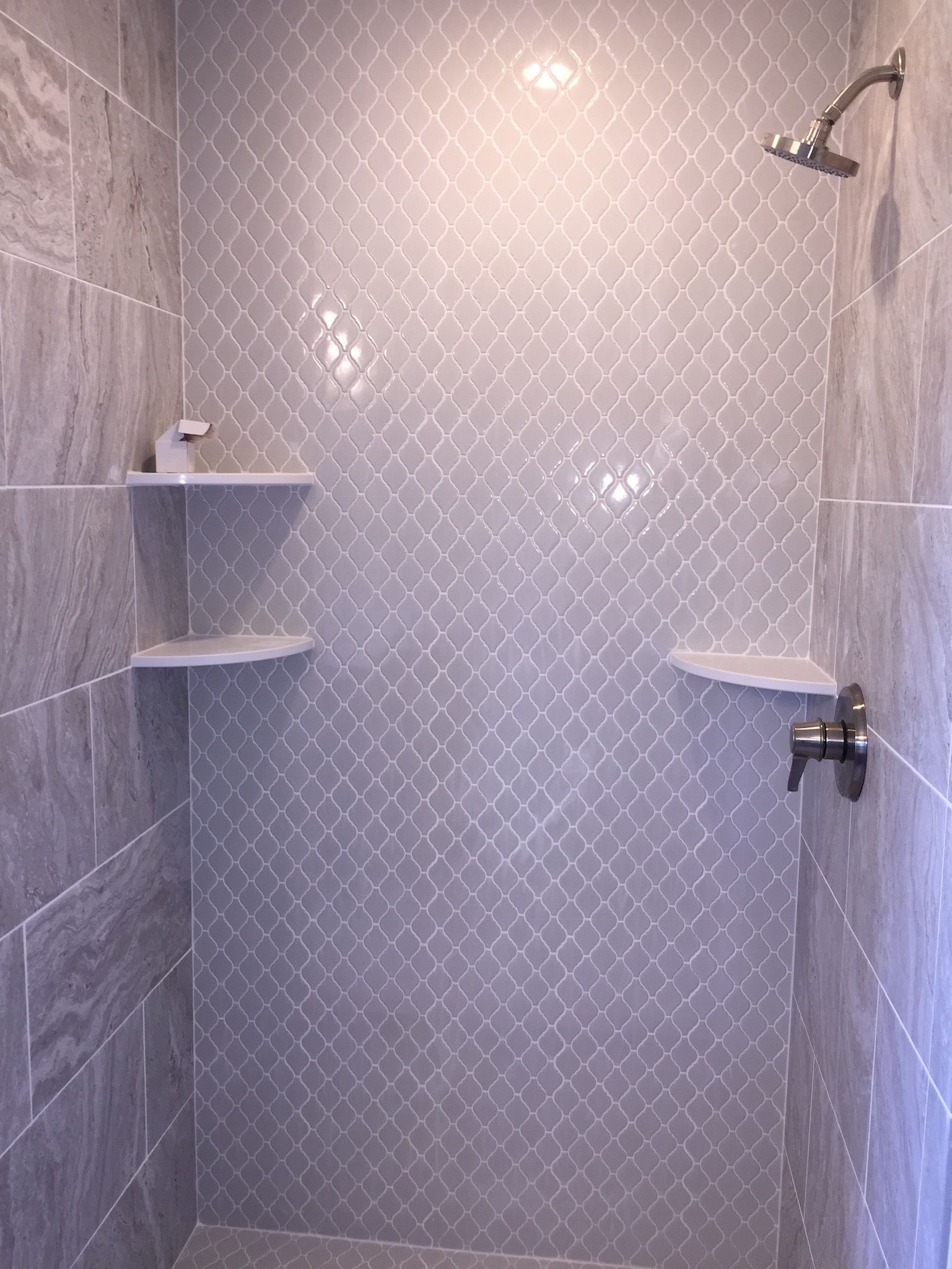 A shower with a shower head and shelves in a bathroom.