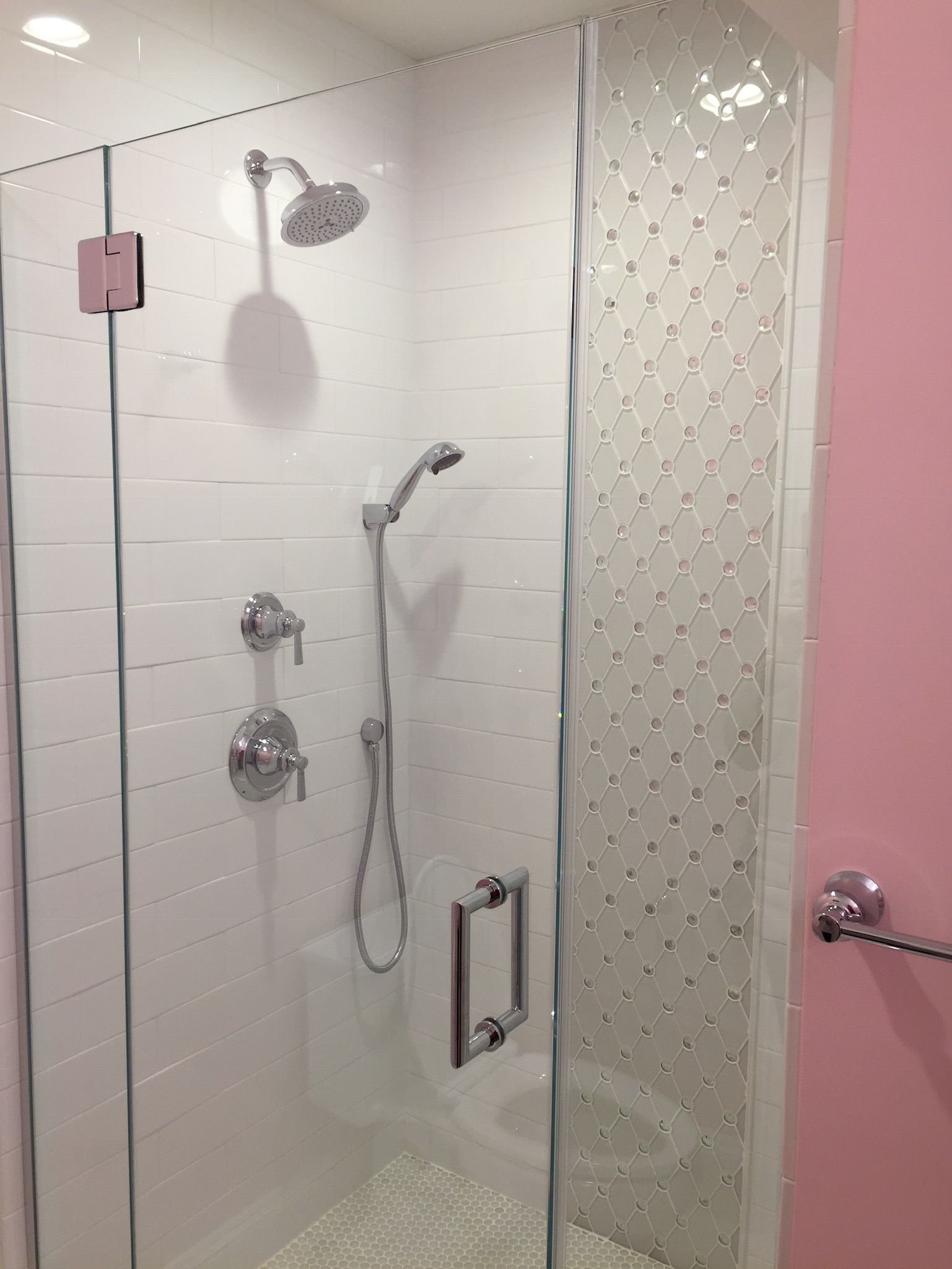 A shower with a glass door and a pink wall.