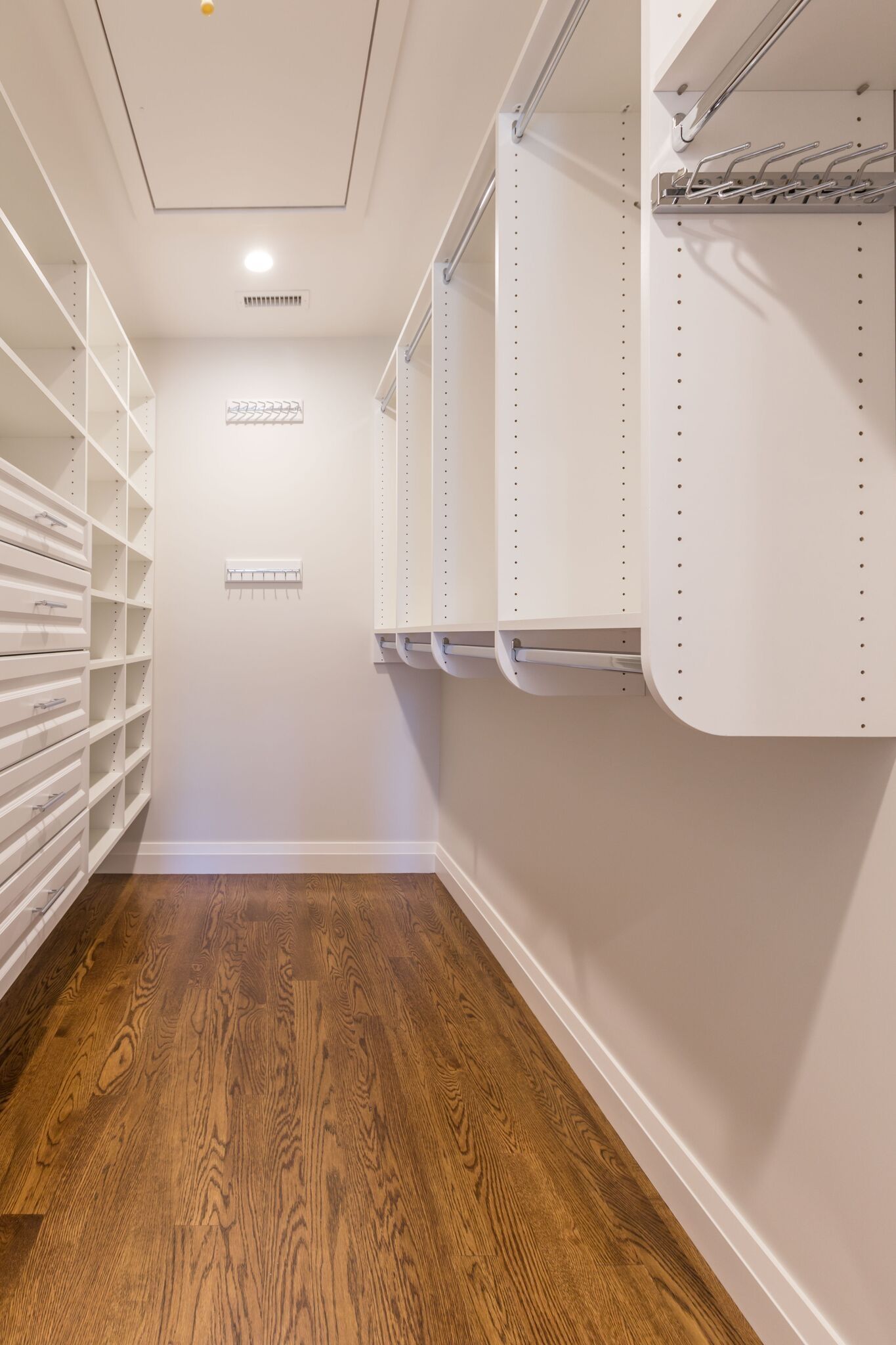A walk in closet with hardwood floors and white shelves.