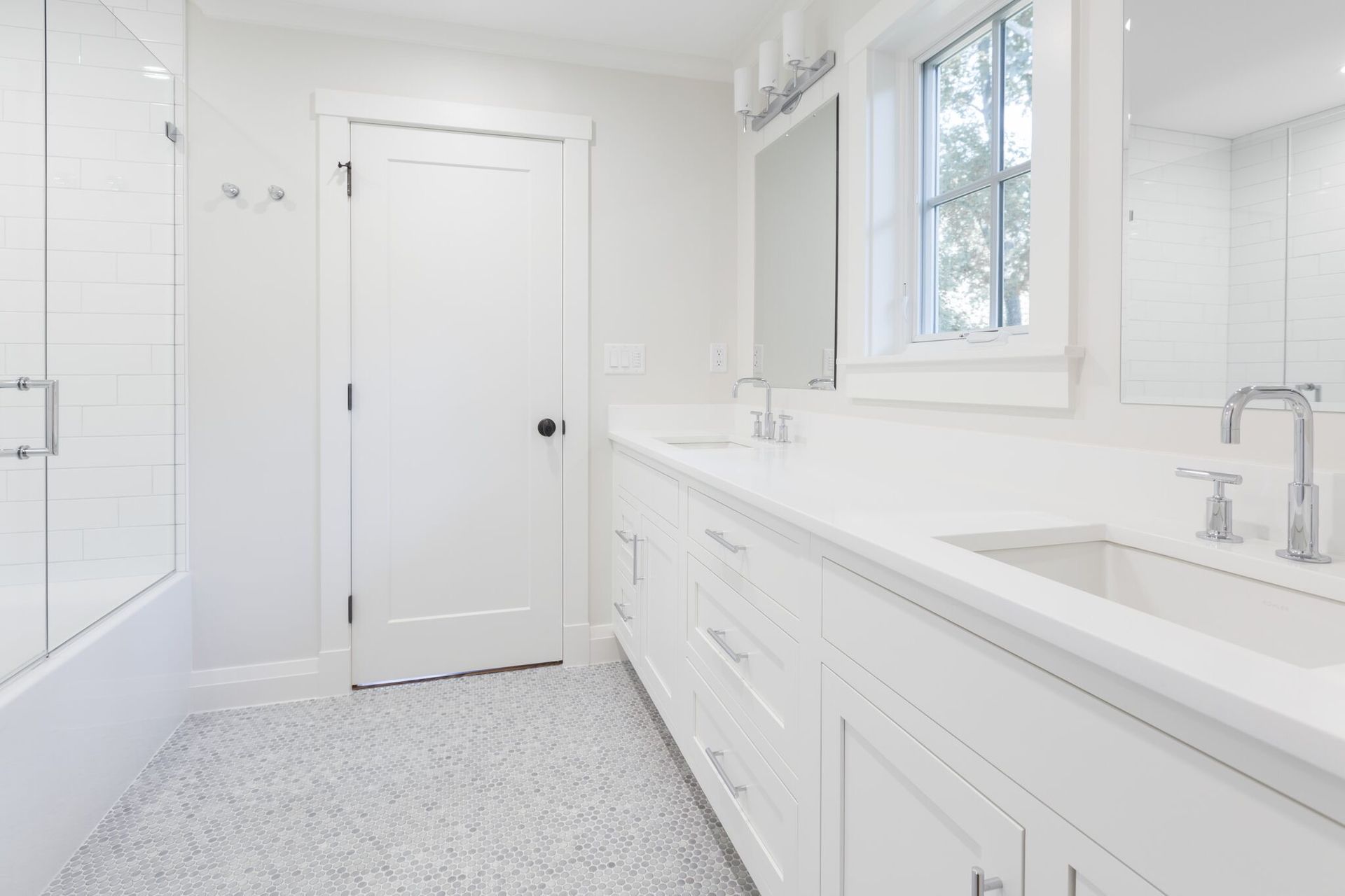 A bathroom with white cabinets , a sink , a mirror and a window.