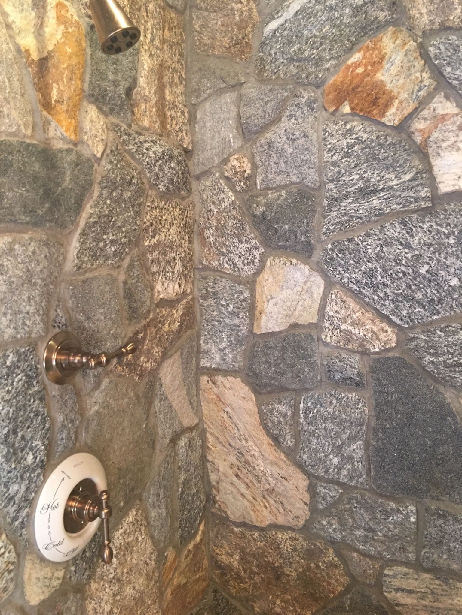 A shower head is hanging from a stone wall.