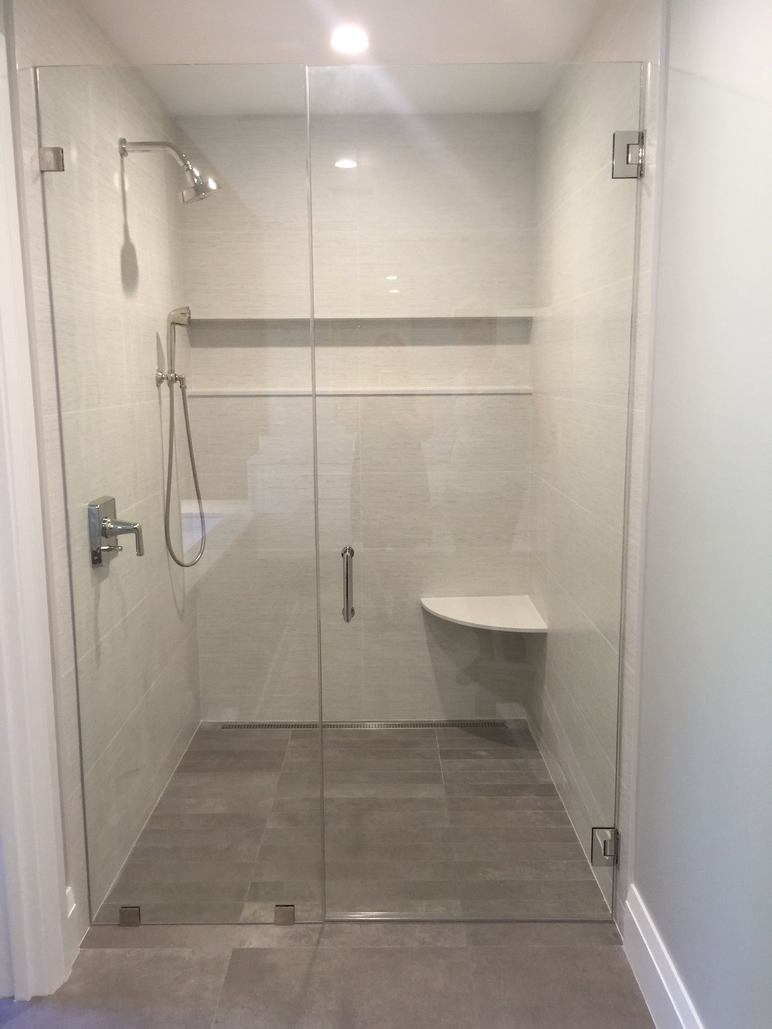 A bathroom with a walk in shower with a glass door and a bench.