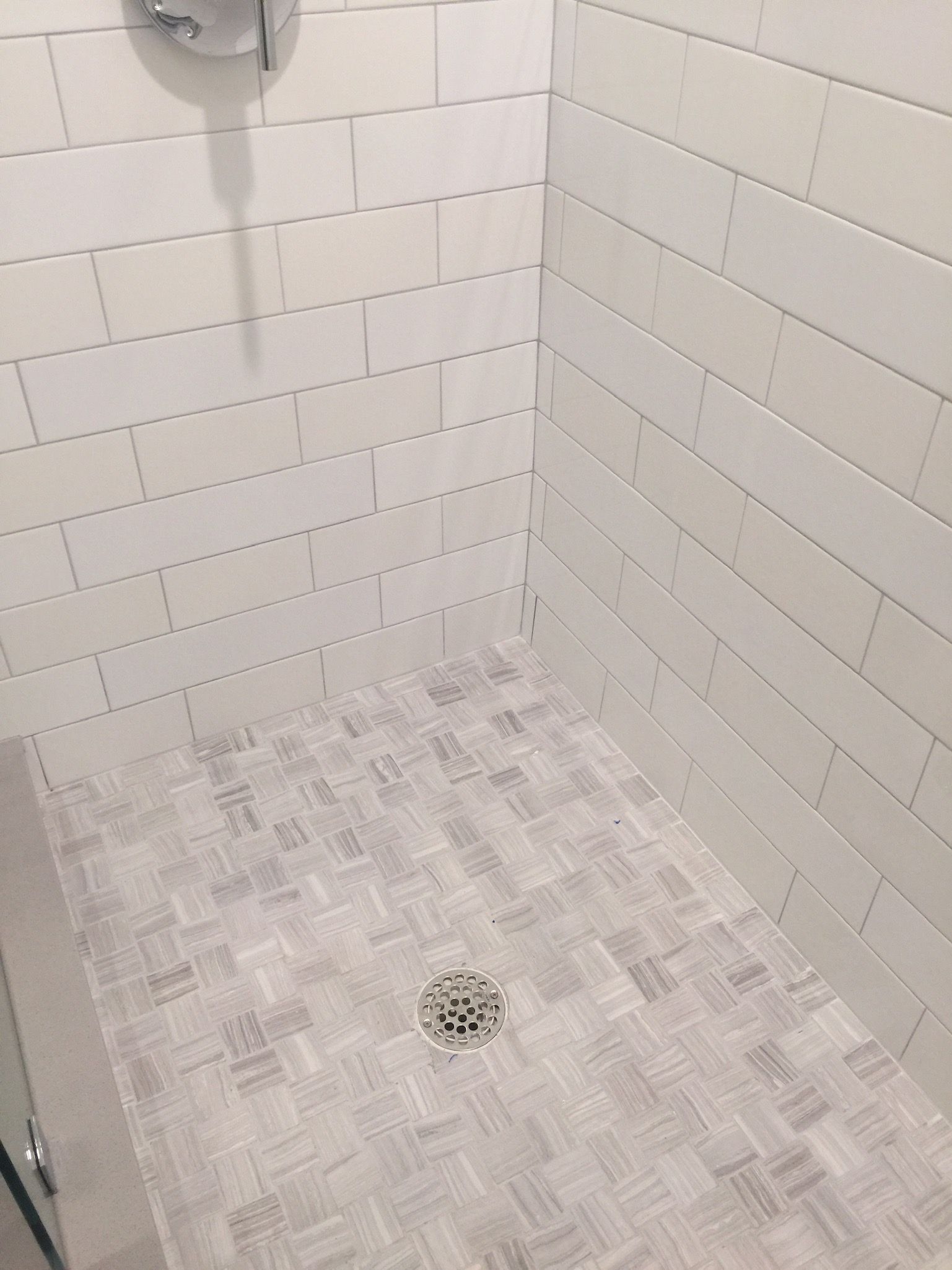A shower stall with white tiles and a drain in a bathroom.