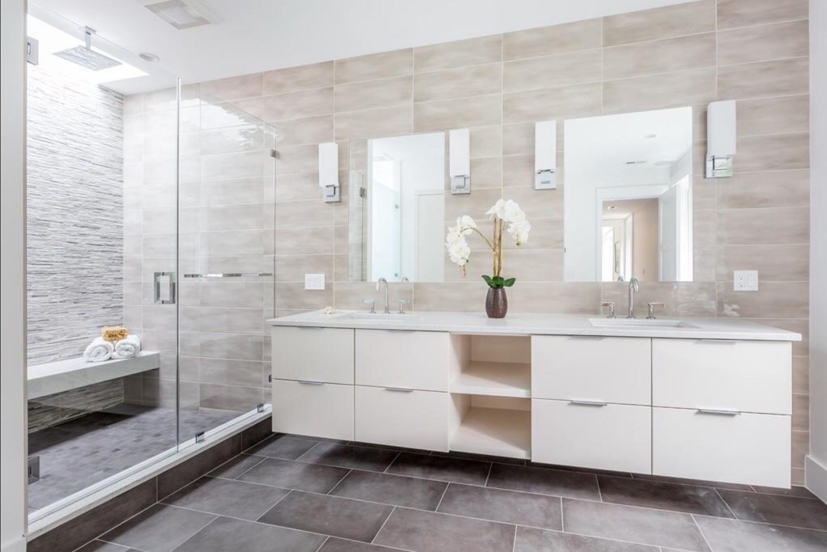 A bathroom with two sinks , two mirrors and a walk in shower.