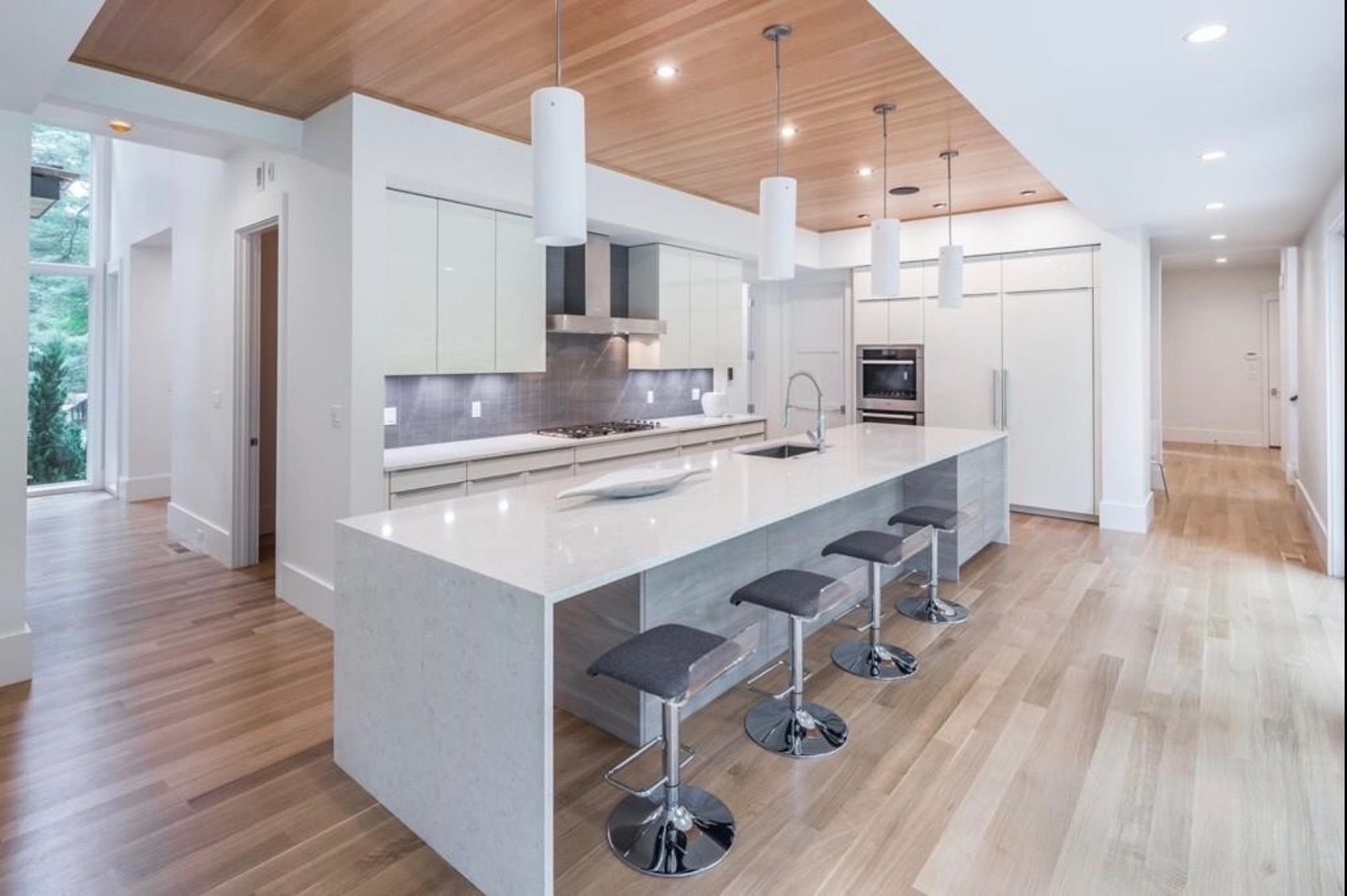 A kitchen with a long island and stools and a wooden floor.