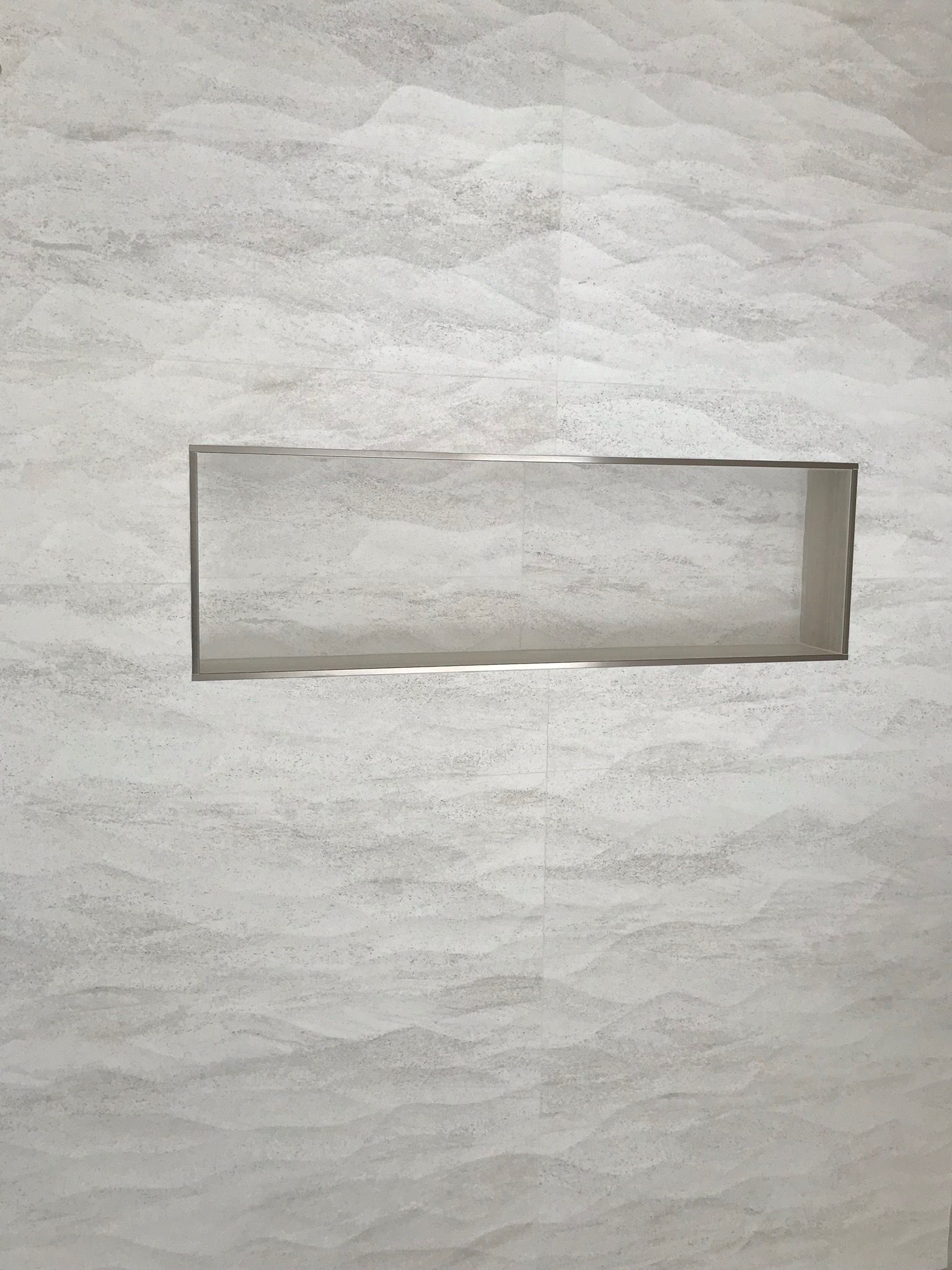 A shower niche in a bathroom wall with a stainless steel frame.