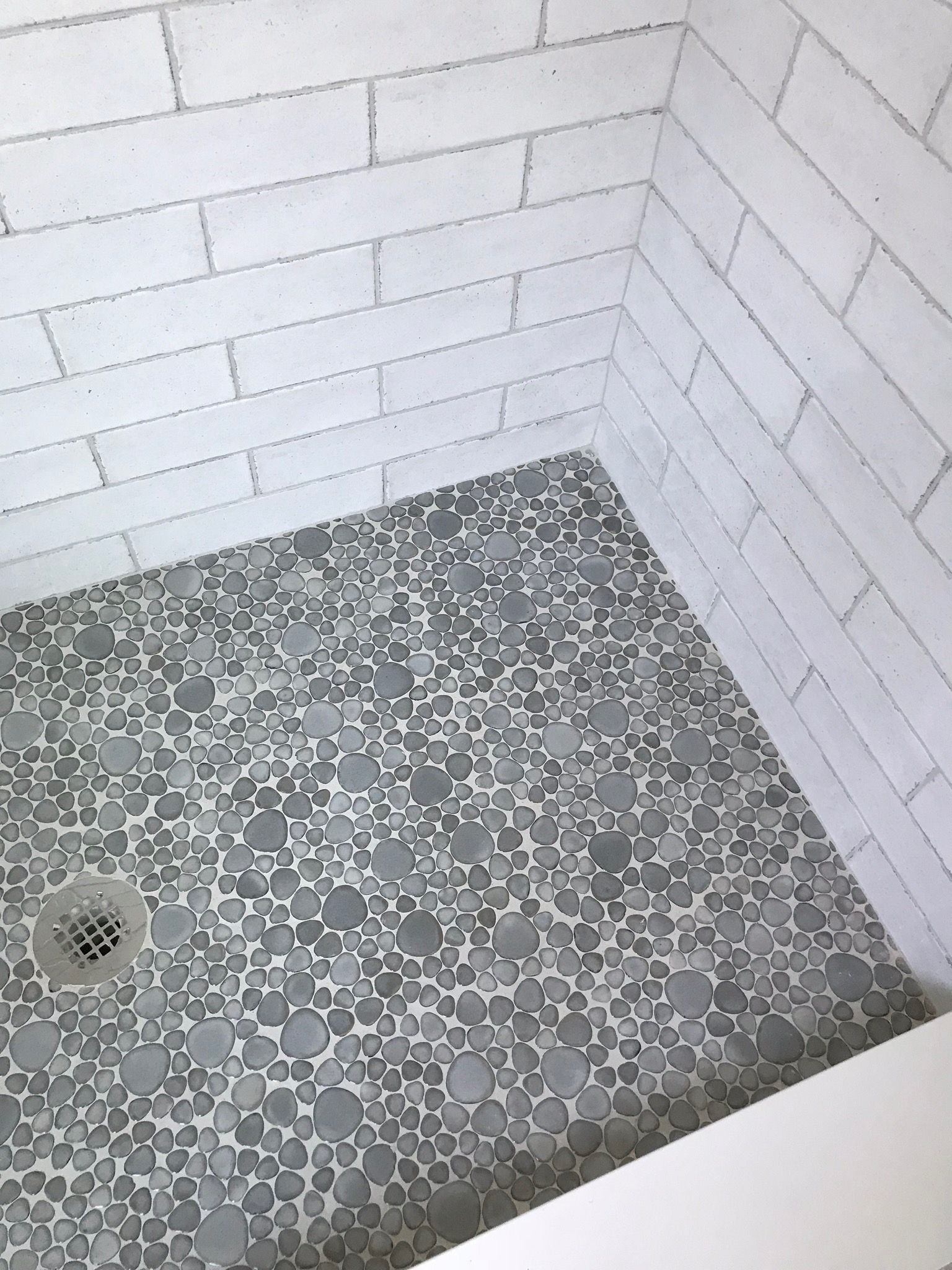 A shower stall with a gray tile floor and white brick walls.