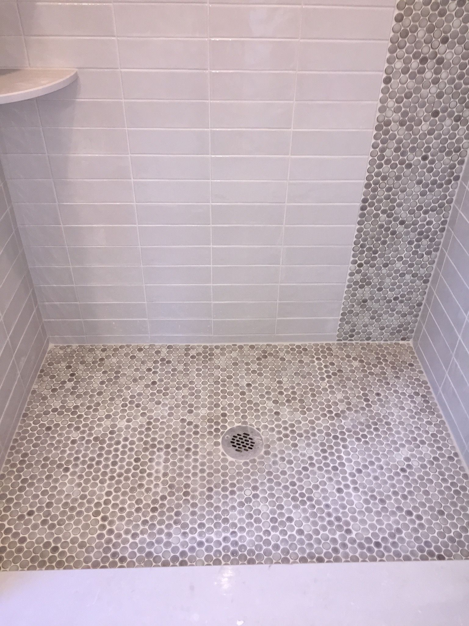 A shower stall with a tiled floor and a drain.