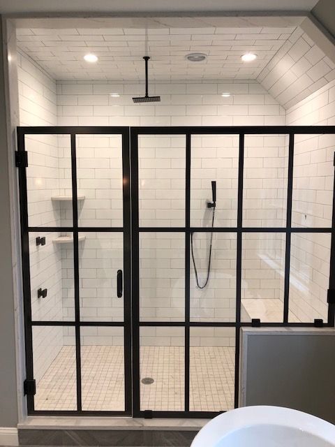 A bathroom with white tiles and a black shower door