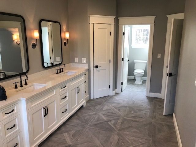A bathroom with two sinks , two mirrors and a toilet.