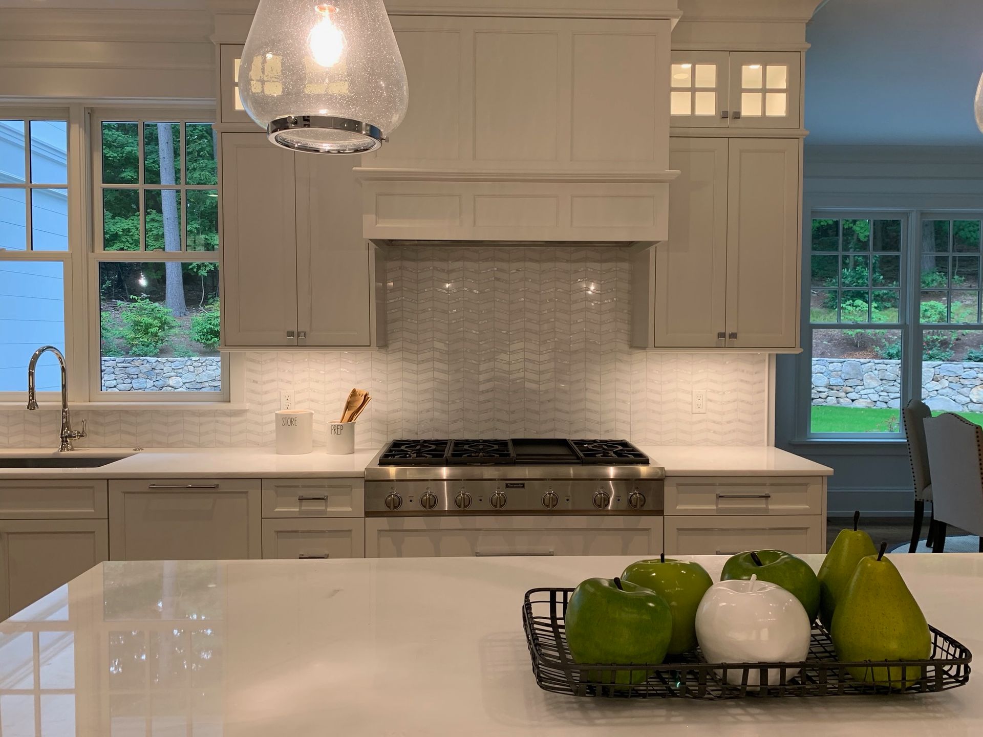A kitchen with white cabinets , a stove , a sink , and a basket of fruit on the counter.