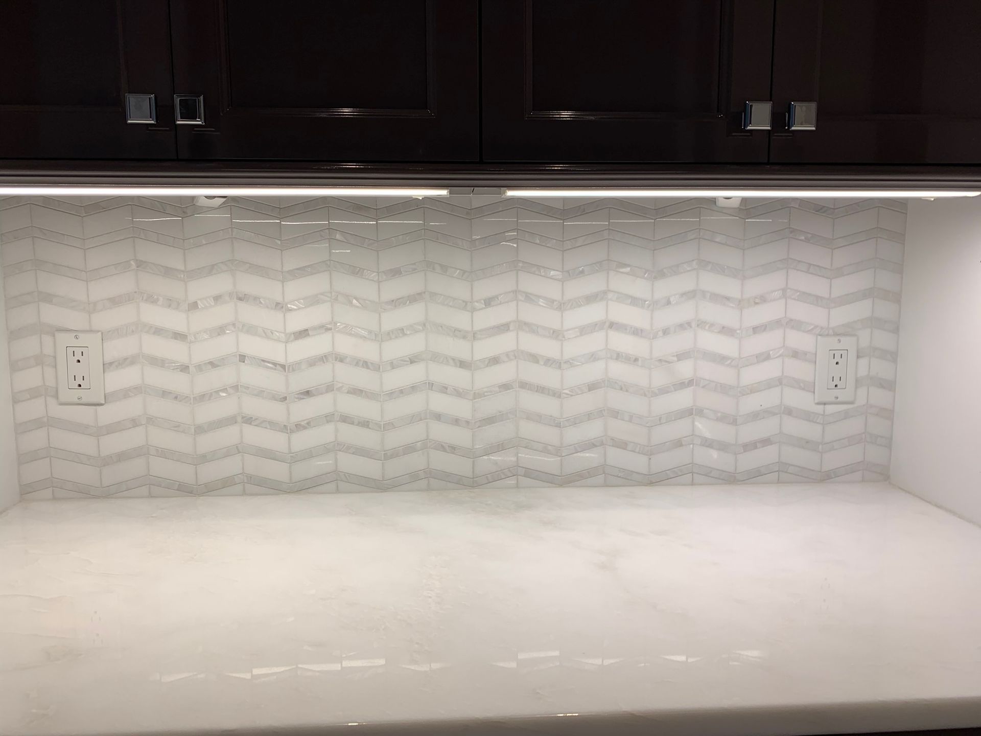 A kitchen with a chevron tile backsplash and a white counter top.