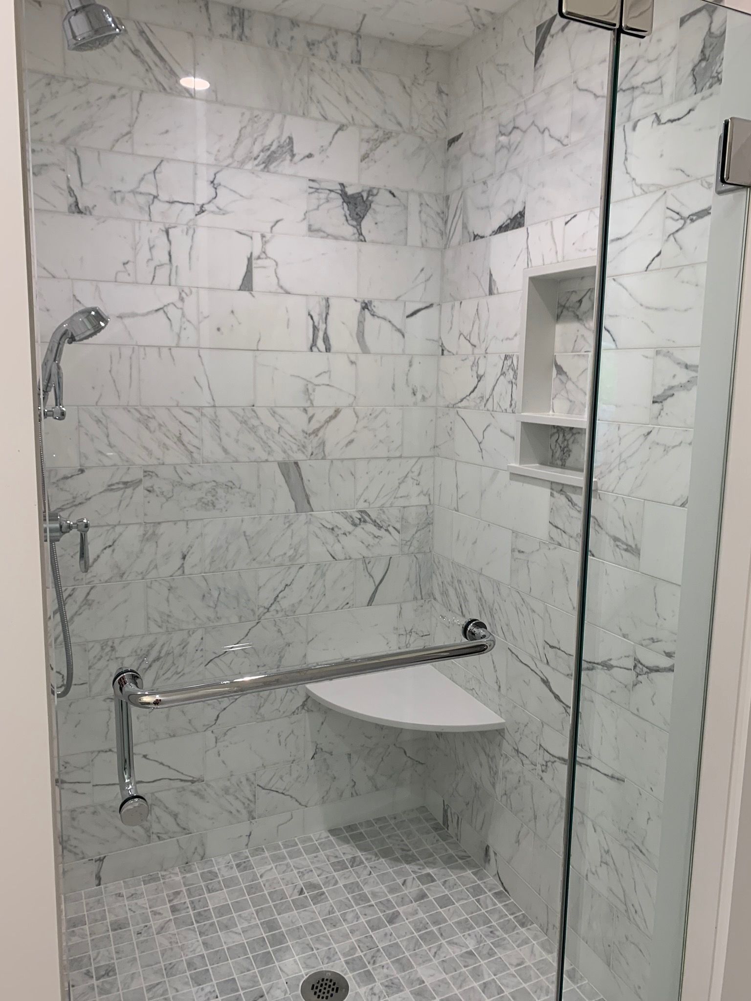 A bathroom with a walk in shower with a bench and a glass door.