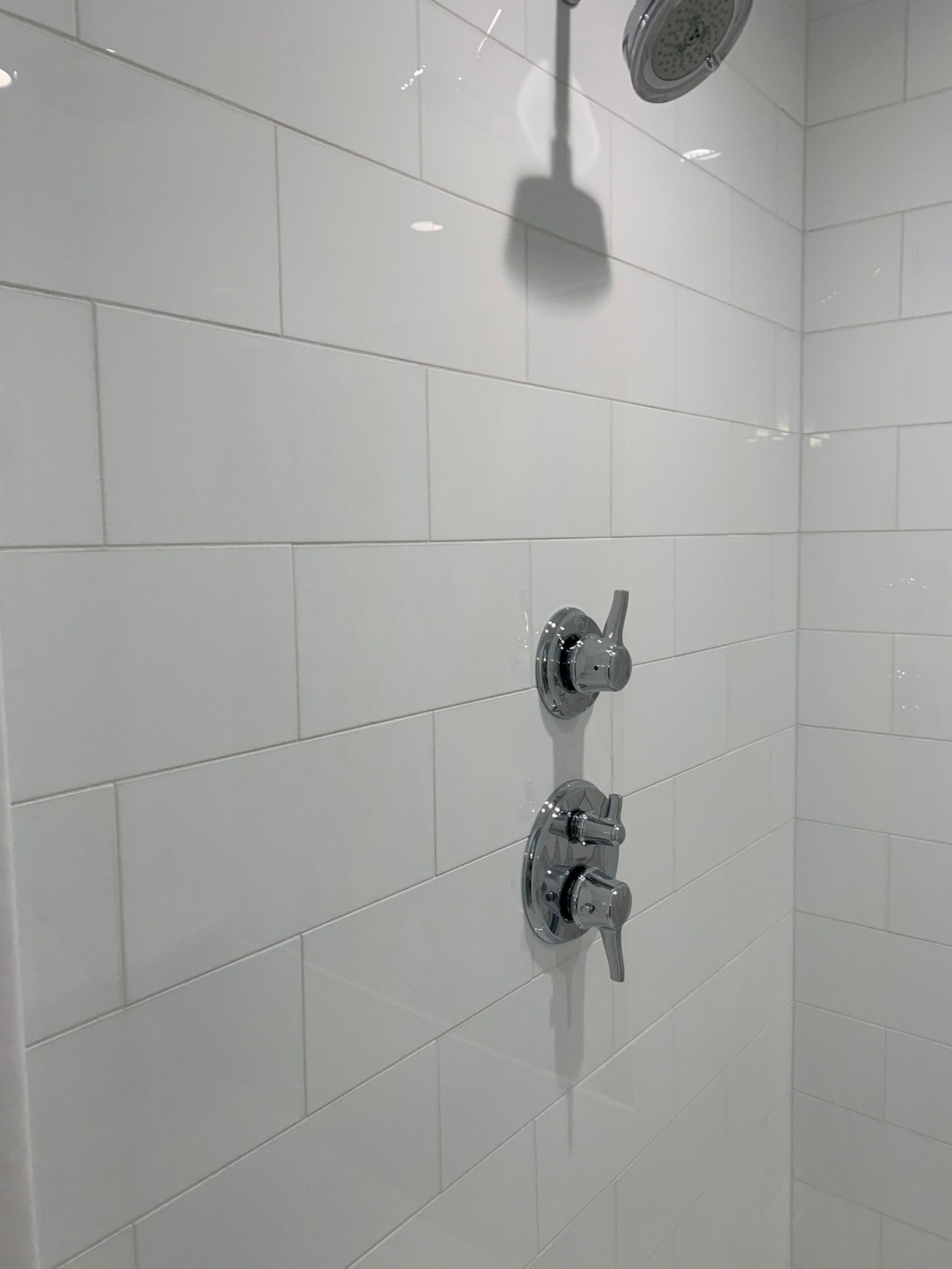There is a shower head in the shower with white tiles.