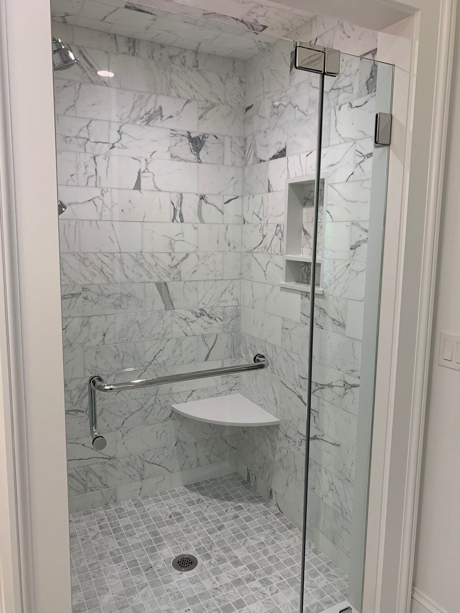 A bathroom with marble tiles and a walk in shower with a glass door.