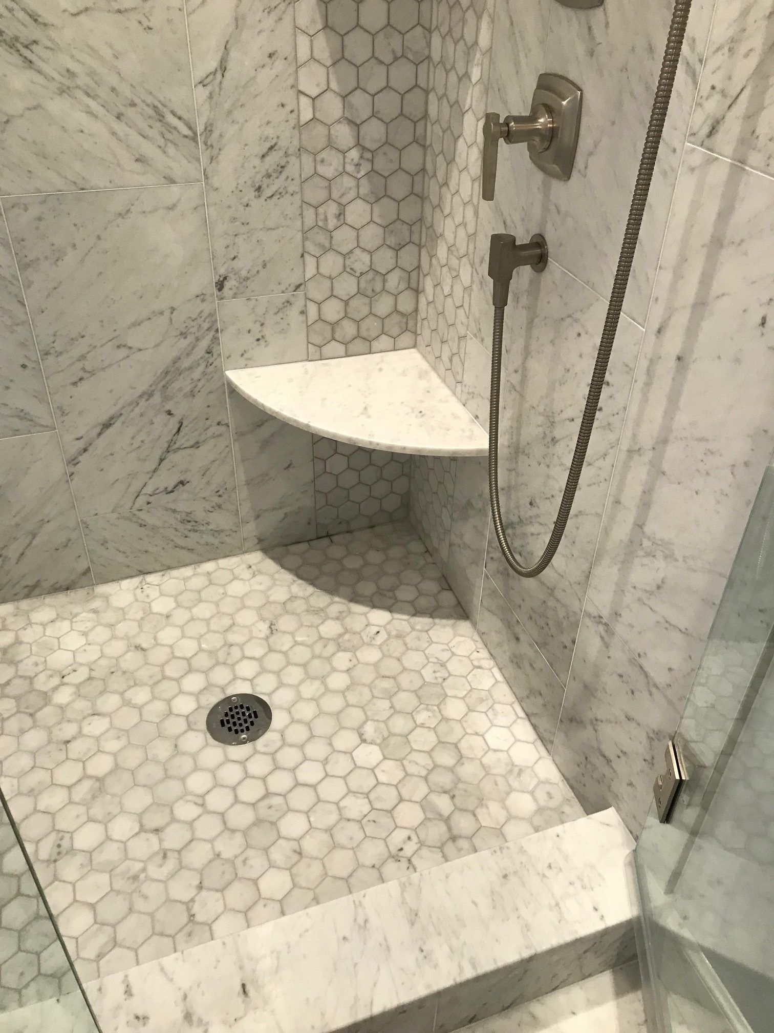 A shower with a seat and a shower head in a bathroom.