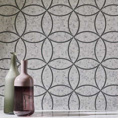 Two vases are sitting on a table in front of a wall with a geometric pattern.