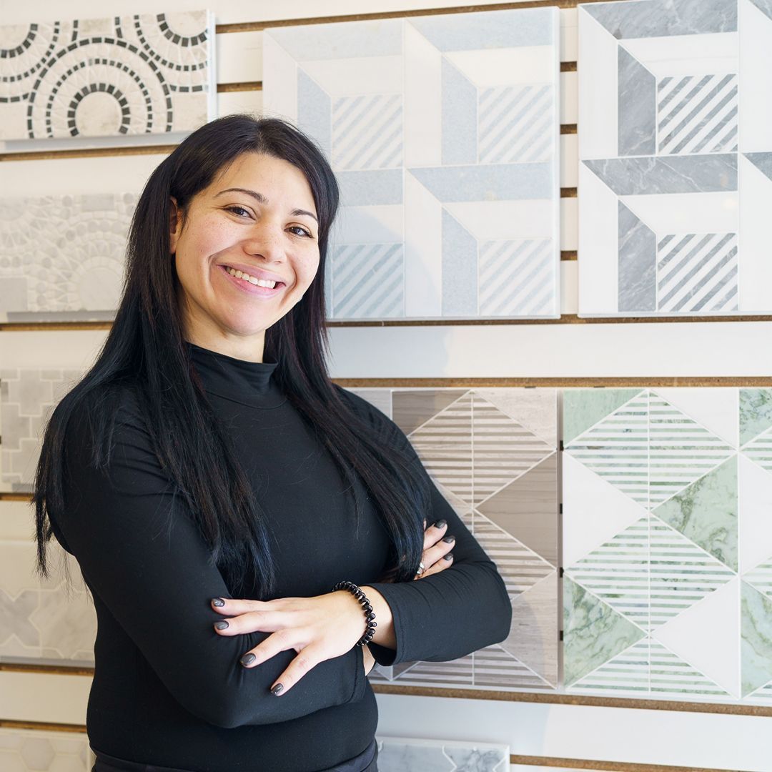 A woman with her arms crossed is smiling in front of a wall of tiles