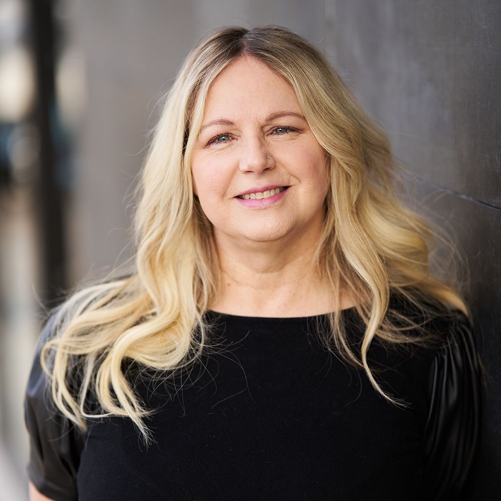 A woman with blonde hair is wearing a black shirt and smiling for the camera.