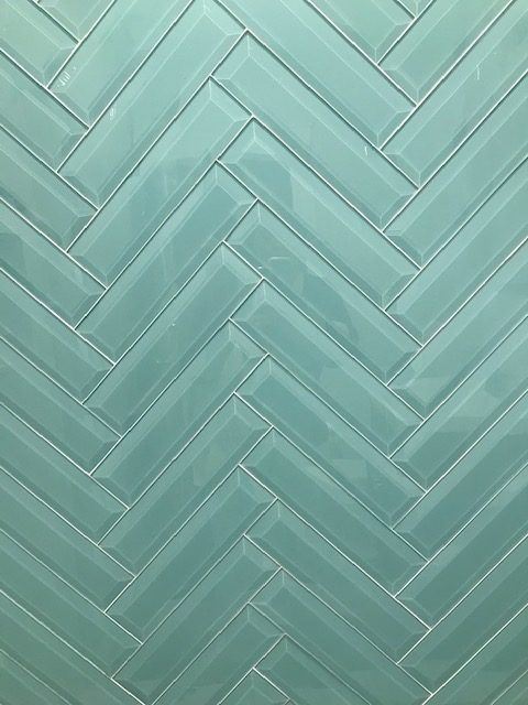 A close up of a green subway tile in a herringbone pattern.