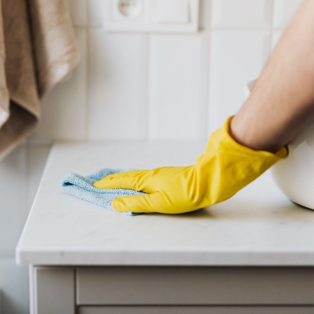 A person wearing yellow gloves is cleaning a counter with a cloth.