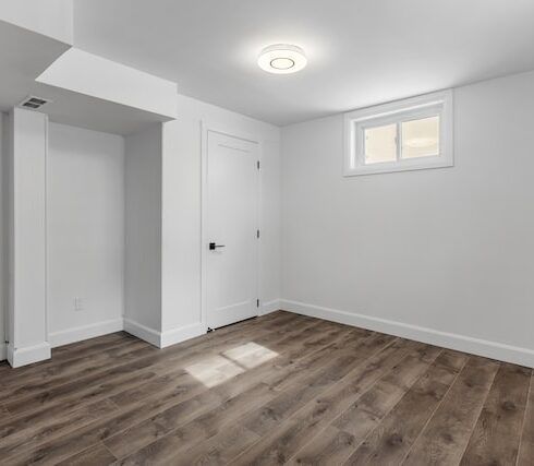 An empty basement with hardwood floors and white walls.