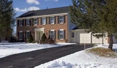 A large brick house with a snowy driveway in front of it