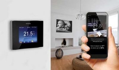 A person is holding a smart phone next to a thermostat in a living room.