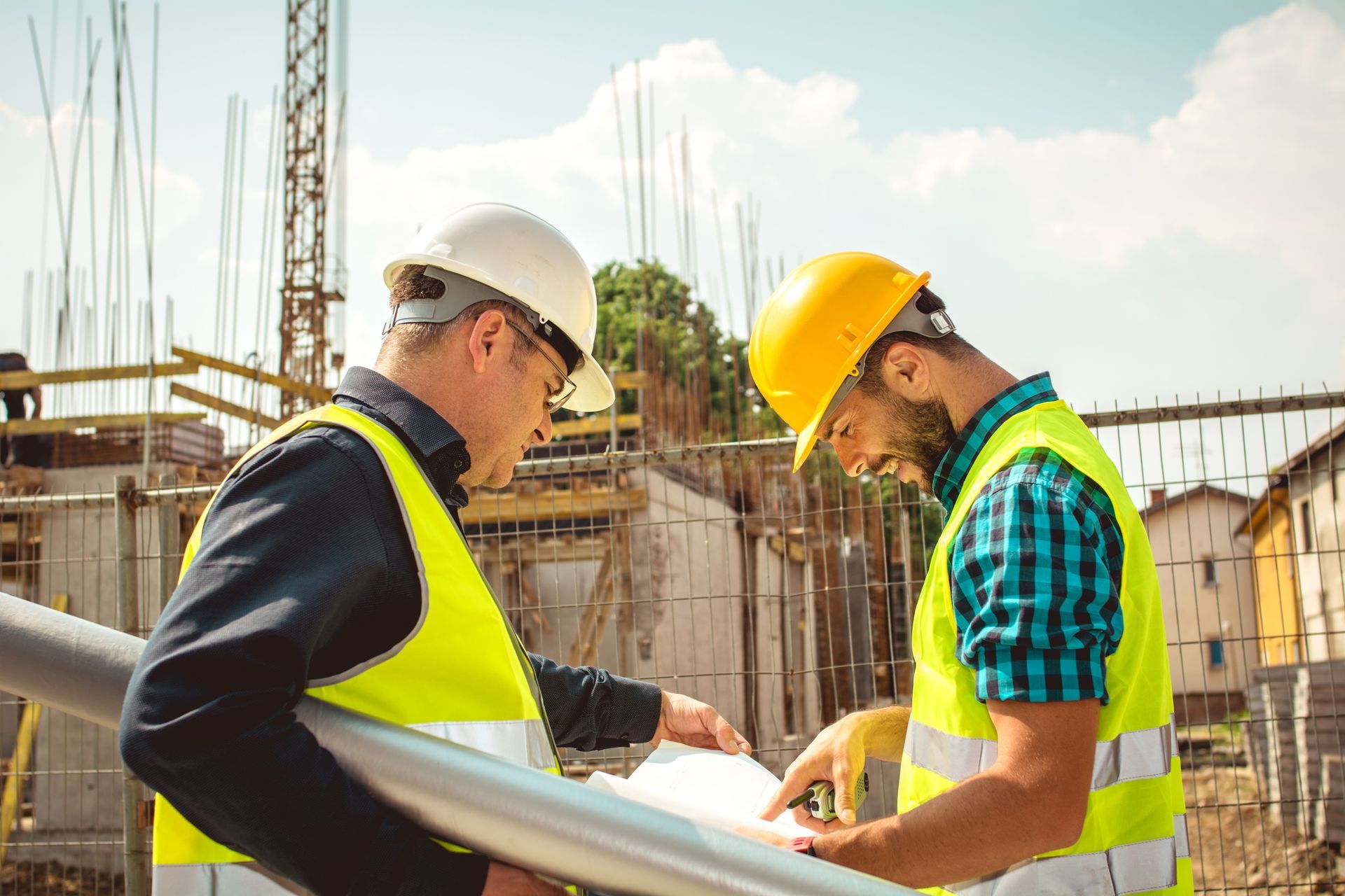Two construction workers reviewing blueprints at a construction site for a new home build project.