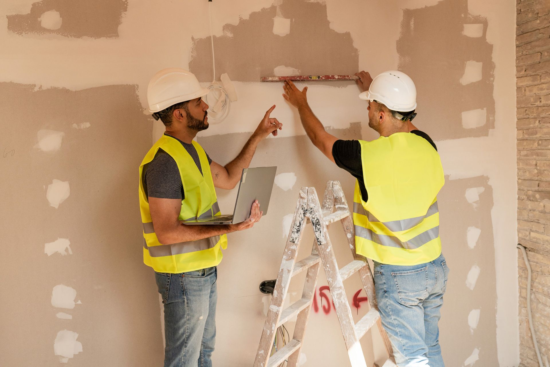 Two workers providing dry wall contractor services in Denver, CO using level and laptop.