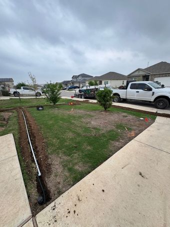 A lawn with a trench dug, white truck parked in front. Cloudy sky.
