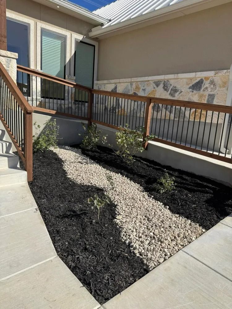 A ramp with railings, mulch, and river rock landscaping.