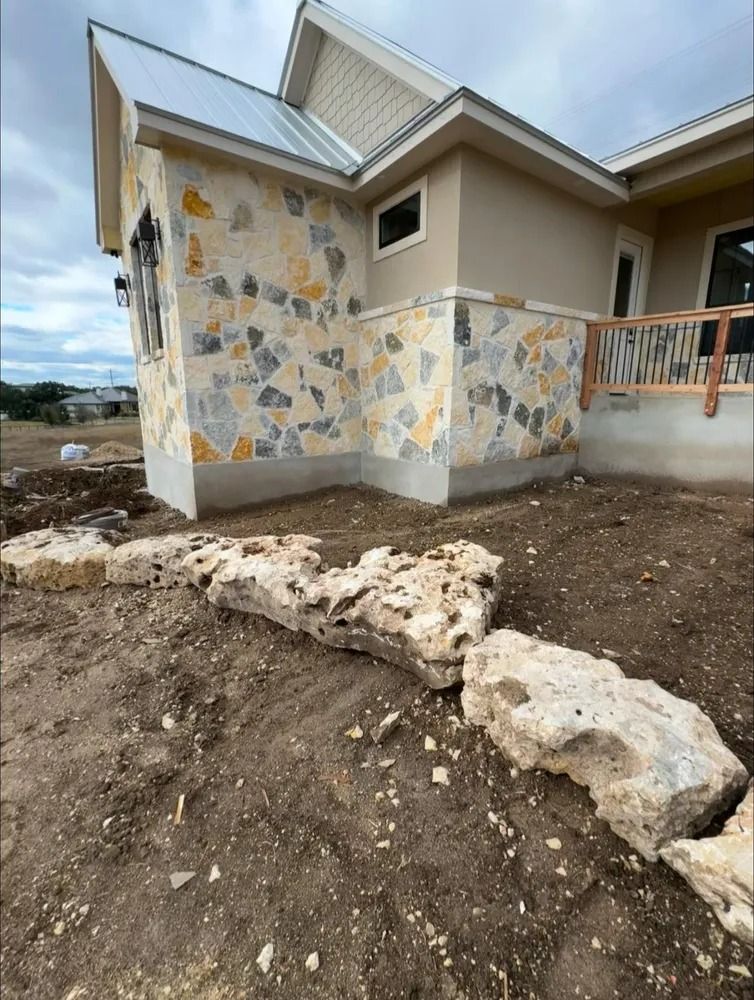 House exterior with stone facade and limestone edging. Dirt foreground. Overcast sky.