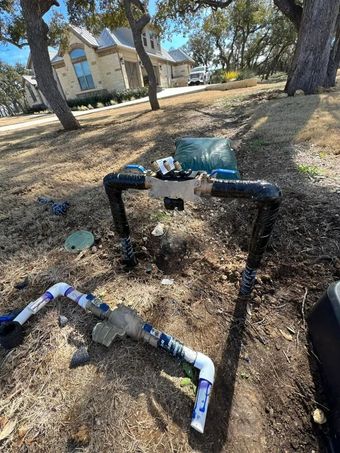 Irrigation system components installed outdoors with PVC pipes and a valve box in a yard setting.