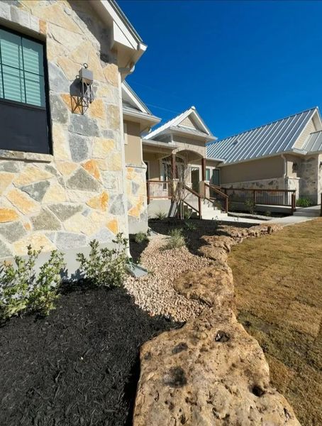 Exterior of a house with stone walls, a small porch, and landscaping with rock and mulch.