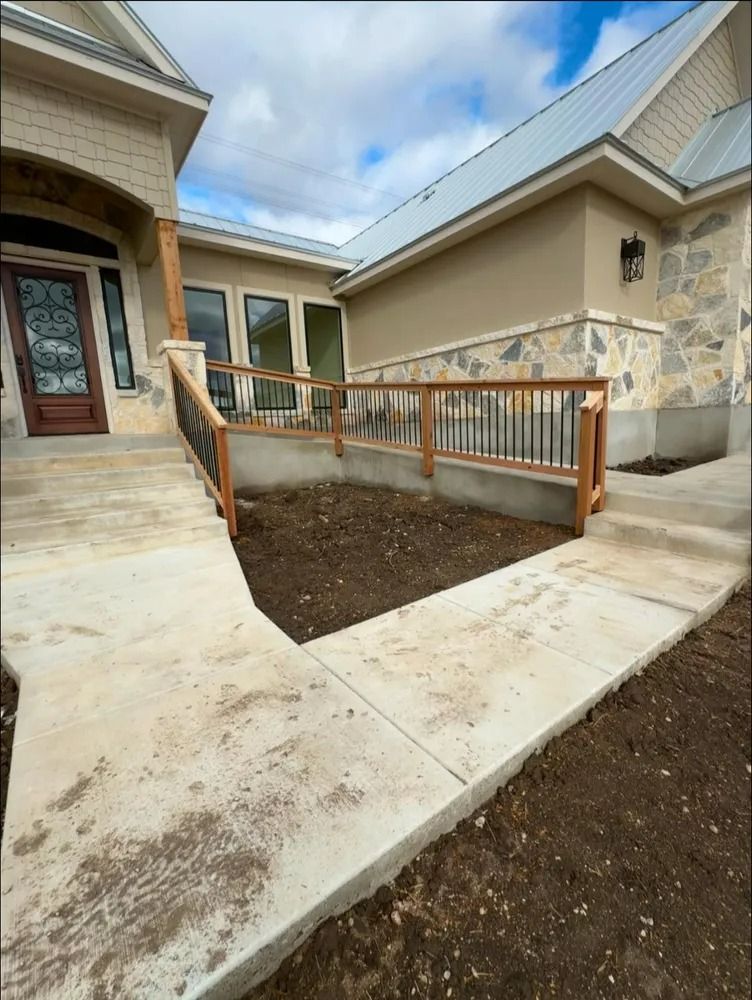 Concrete ramp and pathway leading to a house with a brown door and a ramp with black railings.