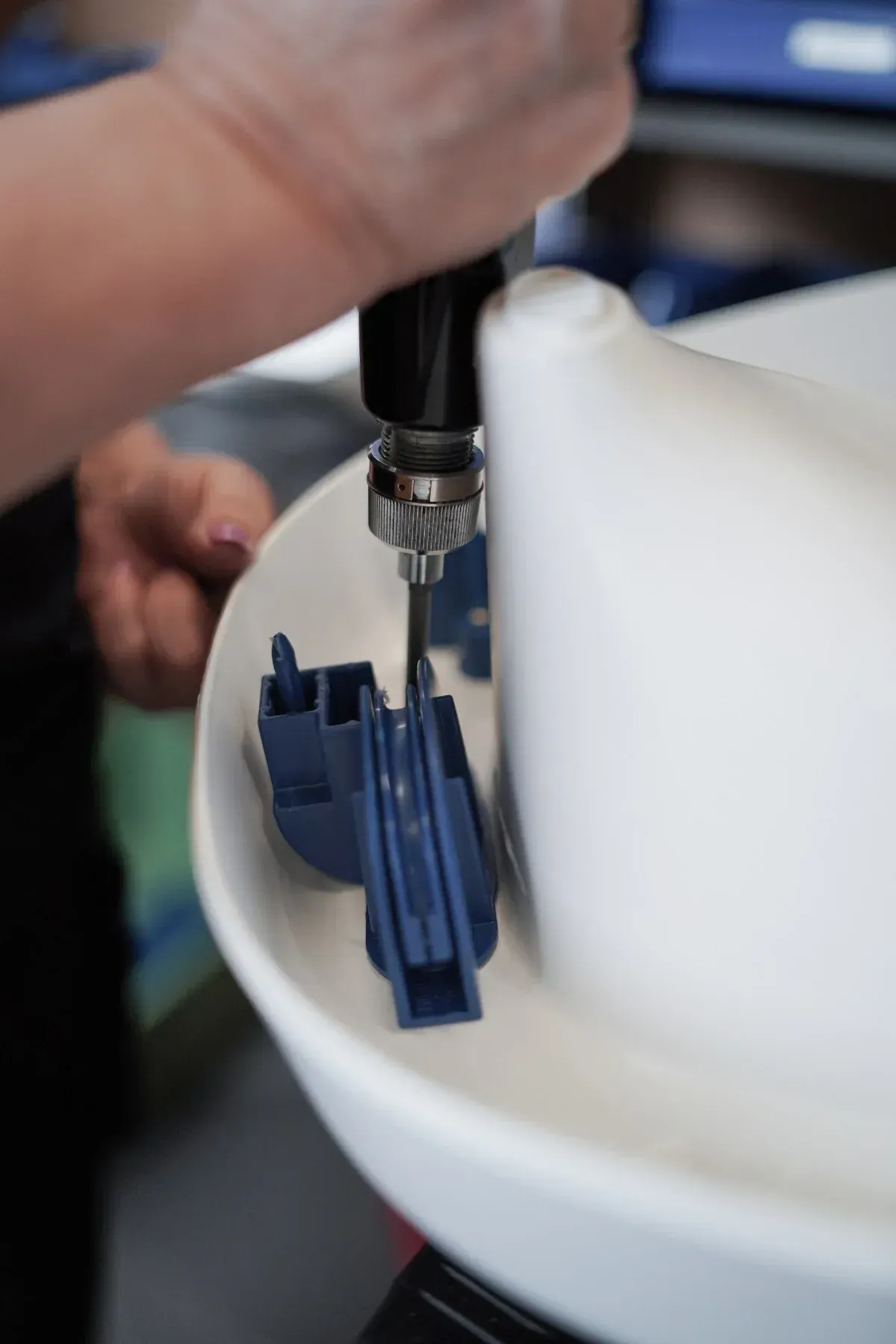 A person uses a power drill to assemble blue plastic components inside a white basin. Close-up shot.