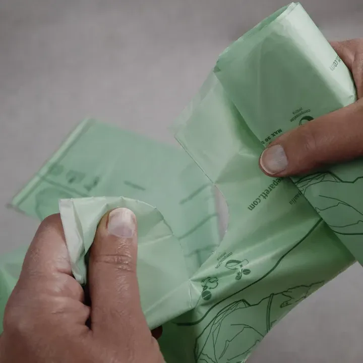 Hands pulling apart a roll of green biodegradable waste bags.