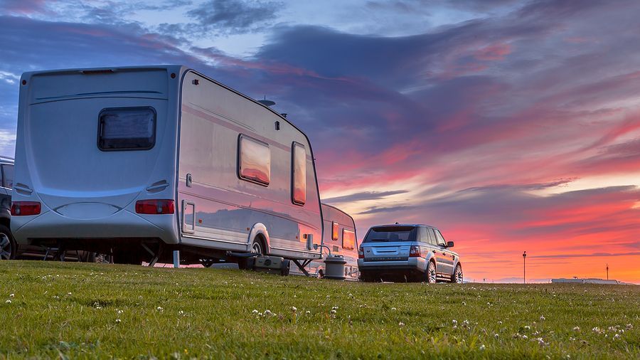 Caravan and SUV parked on grassy hill against vibrant sunset.