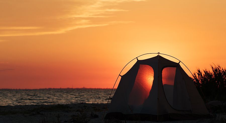 A tent silhouetted against a vibrant orange and red sunset on a beach.
