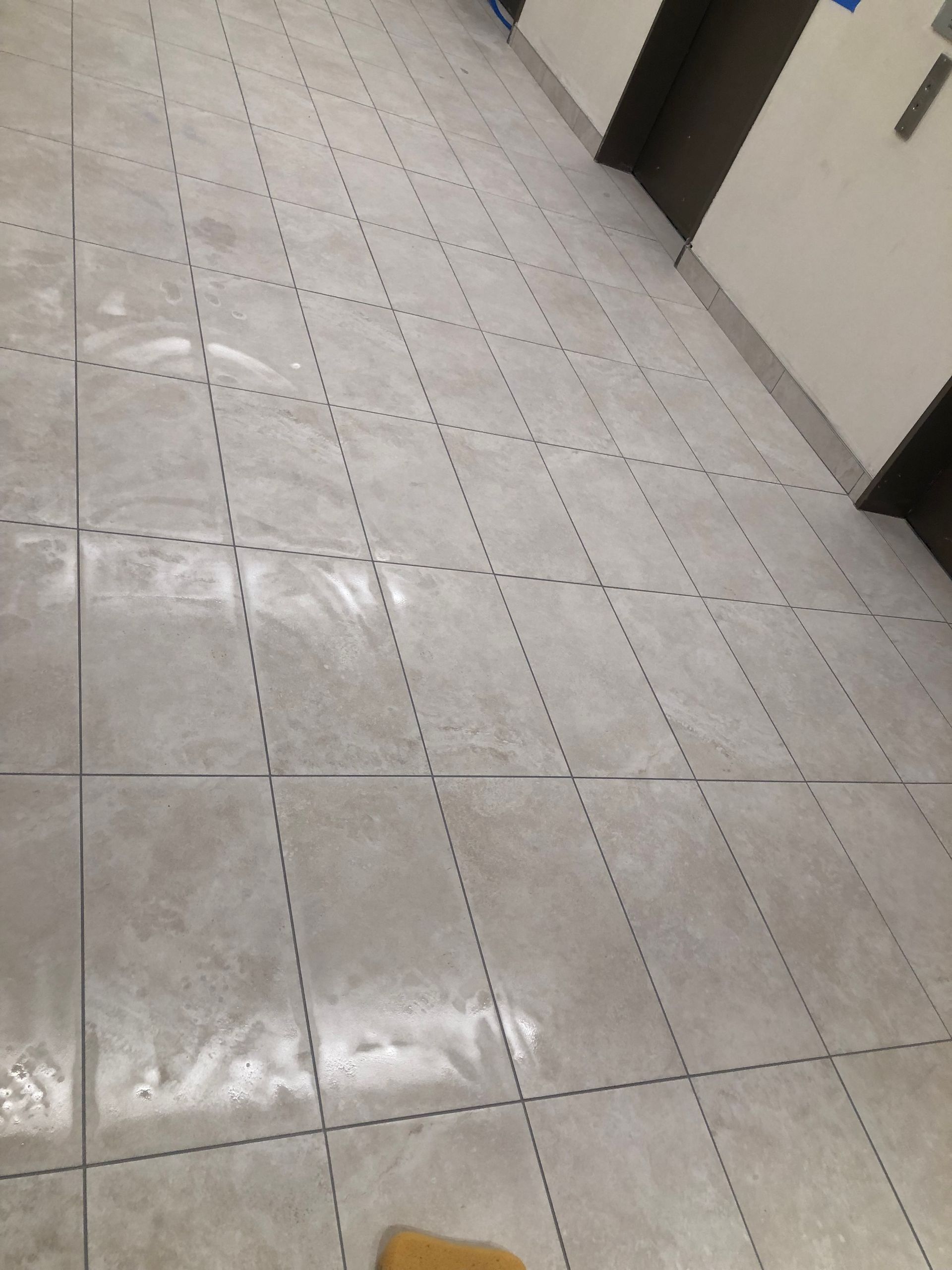 A tiled floor in a hallway with an elevator in the background