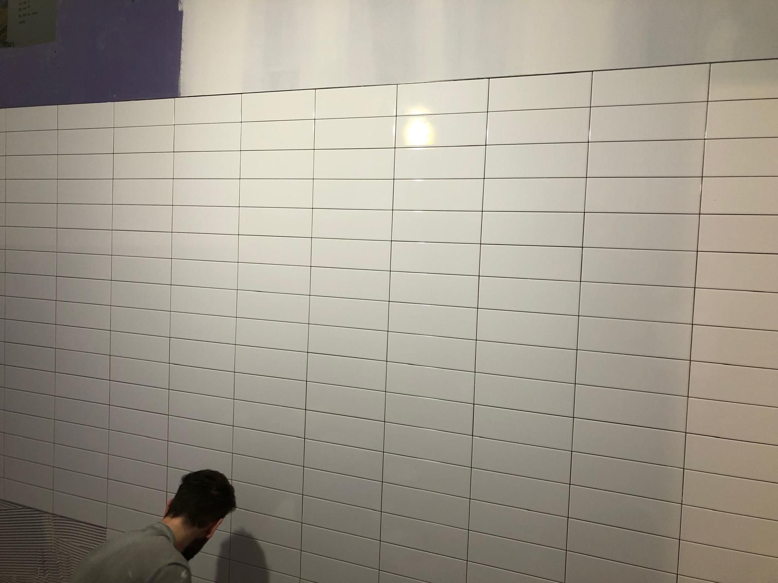 A man is standing in front of a wall of white tiles