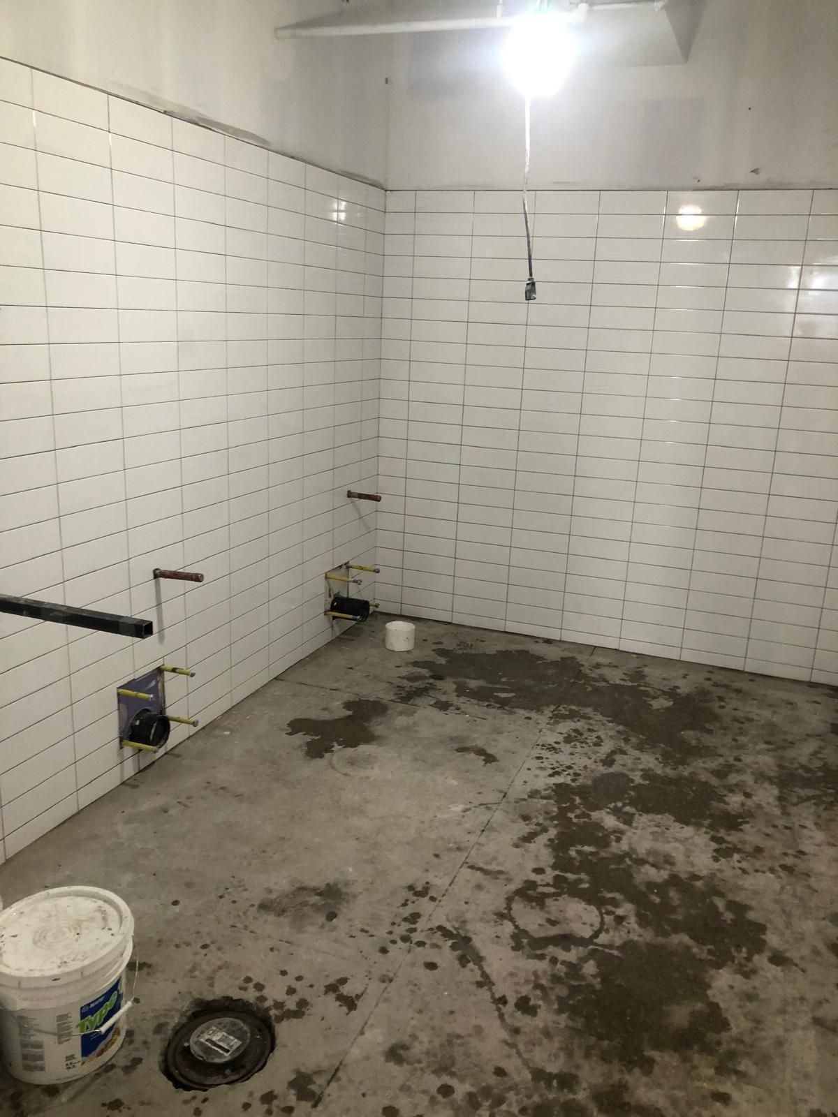 A room with white tiles on the walls and a bucket on the floor.