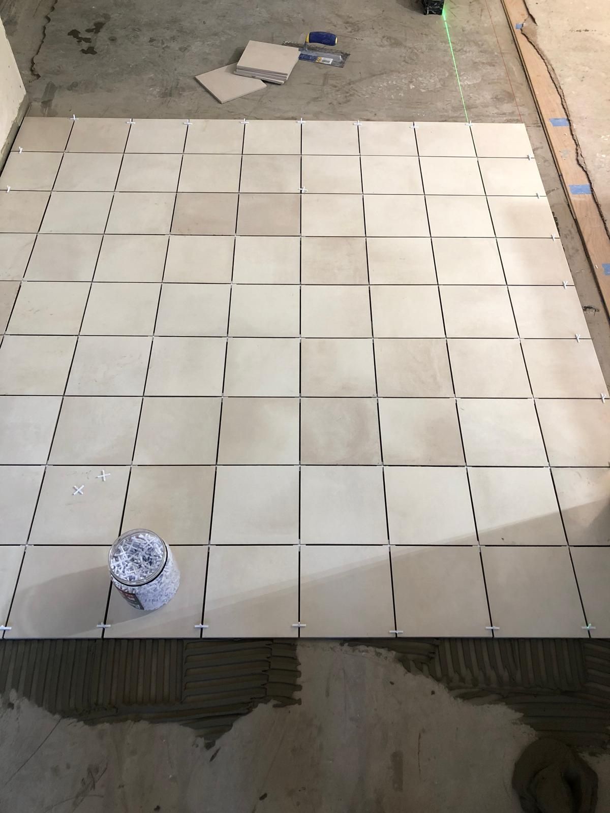 White tiles are being installed on a concrete floor